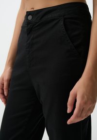 Zwarte katoenen broek met een zachte textuur, voorzien van een knoopsluiting, zijzakken en een op maat gemaakte pasvorm die de taille accentueert.