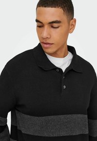 Schwarzes Strick-Polohemd mit strukturiertem Finish, ausgestattet mit einem grauen horizontalen Streifen und drei Knöpfen am Kragen.