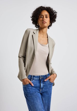 Blazer grigio chiaro su un top beige, abbinato a jeans in denim blu. Il blazer presenta un colletto a risvolto e due bottoni.
