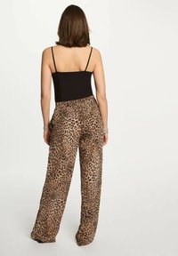 Top nero senza maniche abbinato a pantaloni a gamba larga con stampa leopardata, caratterizzati da una combinazione di colori beige e marrone, texture liscia e vita elastica.