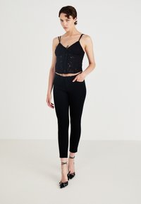 Černý krajkový crop top s nastavovacími ramínky a dekorativním uzlíkem, zkombinovaný s přiléhavými černými kalhotami a puntíkovanými lodičkami.