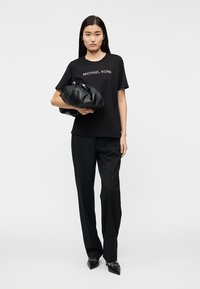 Μαύρο βαμβακερό T-shirt με το λογότυπο "MICHAEL KORS", σε συνδυασμό με μαύρο παντελόνι ραμμένο στα μέτρα και μια μεγάλη μαύρη δερμάτινη τσάντα. Παπούτσια στιλέτο ολοκληρώνουν την εμφάνιση.