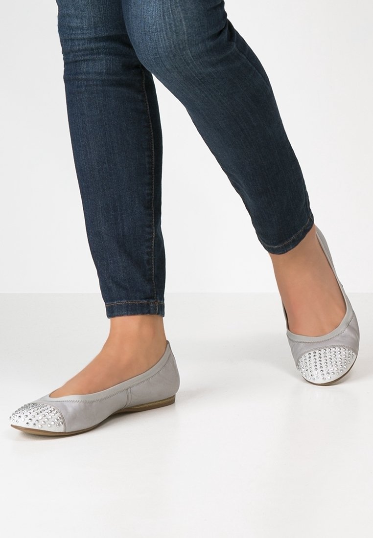 Bailarinas grises con punta redondeada, que presentan una cubierta texturizada de tachuelas plateadas y lados lisos, combinadas con jeans de mezclilla oscura.