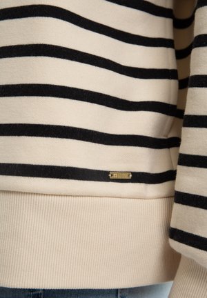 Suéter beige con rayas negras horizontales. Cuenta con puños y dobladillo de canalé, y una pequeña etiqueta dorada cerca de la parte inferior. Textura suave.