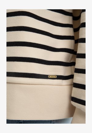 Béžový svetr s vodorovnými černými pruhy. Obsahuje žebrované manžety a lem, a malou zlatou nášivku blízko spodní části. Měkká textura.