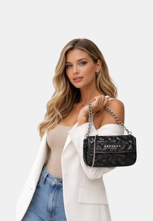 Donna con capelli biondi lunghi indossa un blazer bianco, top beige, jeans blu, tenendo una borsa nera Ermanno con tracolla a catena argentata sulla spalla.