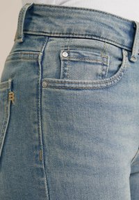 Ljusblå denimjeans med slim fit, synlig sömnad, framficka och detaljer i mässing vid midjan.