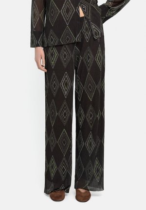 Czarne spodnie o szerokich nogawkach z dużym wzorem diamentu w jasnozielonym i białym kolorze, zestawione z dopasowanym topem i brązowymi płaskimi butami.