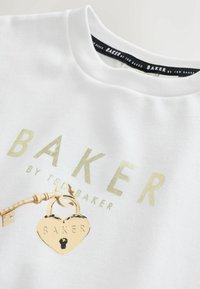 Biela bavlnená mikina s nápisom "BAKER" v zlatej farbe, grafikou zámku a textúrovaným golierom. Dizajn zahŕňa detail kľúča a srdcového zámku.