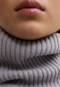 Suéter de cuello alto acanalado en gris claro con una textura gruesa, ajustado alrededor del cuello, que muestra un tejido suave y un patrón uniforme.