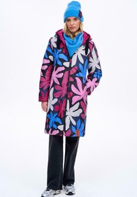 Barevný kabát se vzory a velkými květinovými motivy v růžové, modré a bílé barvě. Obsahuje kapuci a přední zip, doplněný modrou šálou a pletenou čepicí.