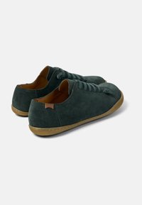 Sneakers in suede di colore verde scuro con punta tonda, suola piatta beige e lacci coordinati. Design minimalista con una texture morbida e un branding discreto.