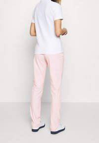 Ljusrosa byxor med en slät yta, med elastisk midja och sidofickor, kombinerat med en vit polo-t-shirt.