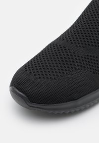 Zwarte sportieve schoen met een ademende mesh bovenkant met een gestructureerd patroon, ronde neus en rubberen outsole met een hanteerbaar ontwerp.