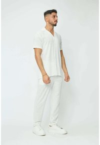 Chemise blanche en lin à manches courtes avec col, associée à un pantalon ajusté assorti. Texture lisse avec un motif rayé subtil. Baskets blanches.