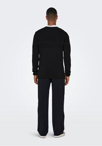 Schwarzer, gestrickter Pullover mit strukturierten horizontalen Streifen. Lange Ärmel, Rundhalsausschnitt, getragen mit lässigen dunklen Hosen und Sneakers. Rückansicht.