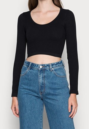 Black ribbed long-sleeve cropped top paired with high-waisted blue denim jeans. The top features a rounded neckline and a fitted design.