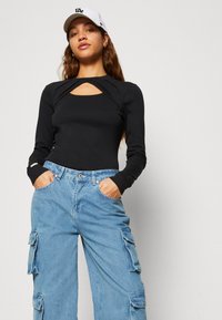 Maglia nera a maniche lunghe con dettaglio a taglio, abbinata a pantaloni cargo in denim azzurro chiaro, larghi, con tasche laterali e vestibilità comoda.