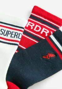 Kolm sokki: valge, punane ja tumesinine. Valgel sokil on mustad ja punased triibud ning kirjutatud on "SUPERDRY". Tumesinisel sokil on punane tiiva logo.