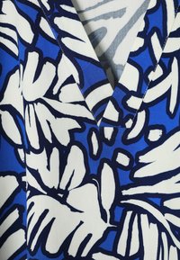 Blåt stof med stort hvidt og mørkeblå abstrakt blomsterprint og V-formet halsudskæringssyning.