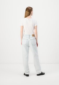 Jeans de tiro alto en azul claro con un ajuste relajado, diseño de cinco bolsillos y una etiqueta de cuero marrón en la parte trasera de la cintura. Camiseta blanca lisa.