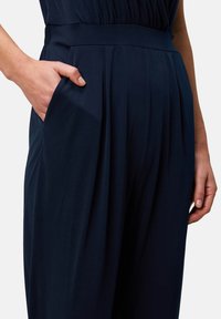 Navy trousers with pleats and an elastic waistband. Features a side pocket; made of smooth, soft fabric with a structured silhouette.