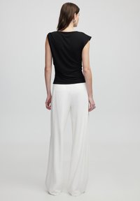 Černý upnutý top s krátkými rukávy, doplněný bílými širokými kalhotami. Hladká tkanina se štíhlým designem a jemným drapáží v pase.