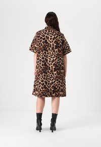 Leopardo raštuotas trumpomis rankovėmis sukienė, pagaminta šviesiai rudos ir rudos spalvų, iki kelių, minkšta tekstūra, derinama su juodais aukštakulniais aulinukais.