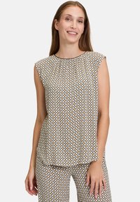 Mönstrad ärmlös topp med ett geometriskt mönster i kräm, brunt och svart. Mjuk tygkvalitet, avslappnad passform och rund halsringning med veck.