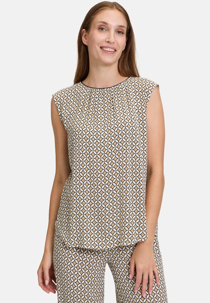 Mönstrad ärmlös topp med ett geometriskt mönster i kräm, brunt och svart. Mjuk tygkvalitet, avslappnad passform och rund halsringning med veck.