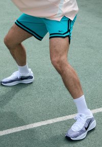 Türkiissinine spordilühikesed püksid mustade triipudega, koos valgete pahkluuni sokkide ja halli ning musta Nike spordijalatsitega rohelisel väljakupinnal.