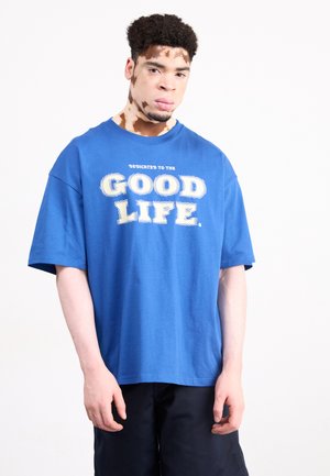 Blue cotton t-shirt with a round neckline and short sleeves, featuring the text "DEDICATED TO THE GOOD LIFE" in white, bold lettering.