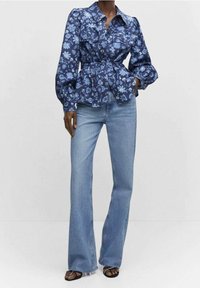 Floral-patterned blue blouse with a fitted waist, puffy sleeves, and a collar, paired with light blue flared jeans and black sandals.