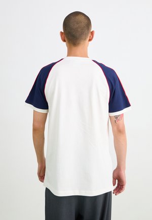 Kurzarm-T-Shirt mit weißem Körper, marineblauen Schultern und roten Nähten. Aus weichem Baumwollmaterial, mit Rundhalsausschnitt und lockerer Passform.