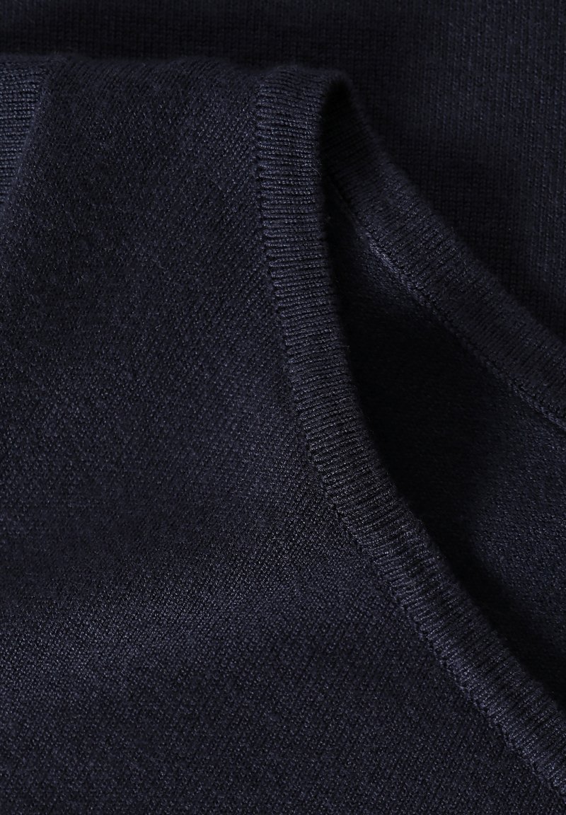 Granatowa dzianina o gładkiej teksturze, z prążkowanym dekoltem i subtelnym diagonalnym wzorem, prezentująca miękki i elastyczny materiał.