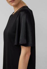 Czarna bluzka z krótkimi, rozkloszowanymi rękawami, o satynowej teksturze, z okrągłym dekoltem i dekoracyjnym wykończeniem na krawędzi.