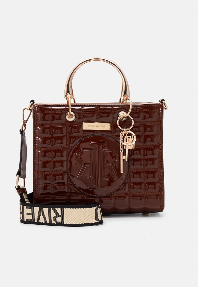 Sac à main brun foncé brillant avec motif matelassé, poignées dorées, breloques décoratives en forme de clés et une bandoulière beige avec le texte "RIVER ISLAND".