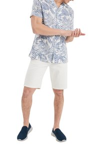 Camisa de botones de manga corta con un patrón de hojas azules, combinada con pantalones cortos blancos y zapatos de lona azul marino. Tejido suave, corte relajado.