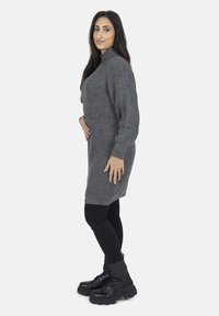 Grå ribbede sweaterkjole med lange ærmer og høj hals, parret med sorte leggings og kraftige sorte snørrebåndsstøvler.