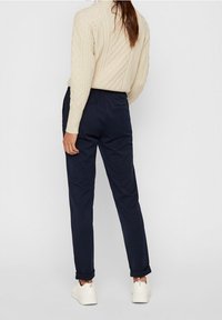 Beige cable-knit sweater paired with dark navy trousers. Trousers feature a relaxed fit and rolled cuffs, worn with white sneakers.