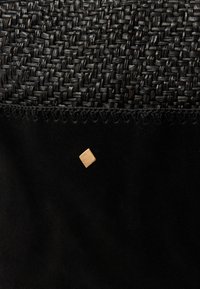 Schwarzer gewebter Stoff mit einem glatten, schwarzen Wildledersockel. Verfügt über ein kleines, quadratisches goldfarbenes Akzent auf der Seite mit dekorativen Stichen entlang des Randes.