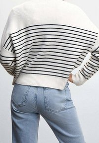 Maglione lavorato a maglia color crema con strisce navy, caratterizzato da una vestibilità comoda e orlo a coste. Abbinato a jeans in denim di un leggero blu con tasche posteriori.