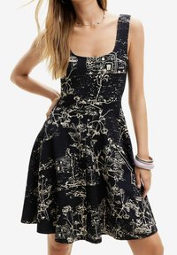 Robe noire avec un corsage ajusté et une jupe évasée, ornée d'un design floral et de motifs de maison en beige. Tissu lisse avec un décolleté carré.