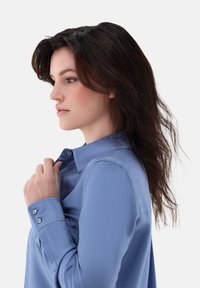 Light blue long-sleeve shirt with a collar, featuring button cuffs and a smooth, shiny texture. Styled with a relaxed fit.