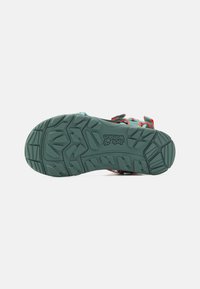 Footwear with a textured green rubber sole, featuring red and blue straps and a buckle, designed for outdoor use.