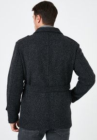 Cappotto grigio a fantasia realizzato in materiale testurizzato, dotato di una cintura in vita, ampio colletto e spalline sulle spalle.