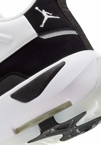 Nærbillede af sålen på en sort og hvid atletisk sneakers med synlig dæmpning og broderet Jumpman-logo nær hælen.