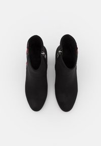 Paire de bottines noires avec fermetures éclair latérales et broderie florale rouge, vues de dessus sur fond blanc.