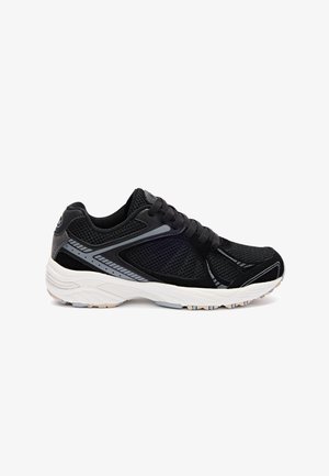 Zapatilla deportiva negra con detalles en gris, paneles de malla, suela blanca acolchada y cordones negros, mostrada de perfil sobre fondo blanco.
