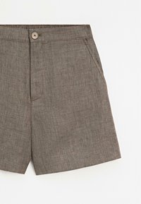 Bruine, gestructureerde stoffen shorts met een knoop aan de voorkant, ritssluiting, zijzakken en elastische tailleband op een effen witte achtergrond.
